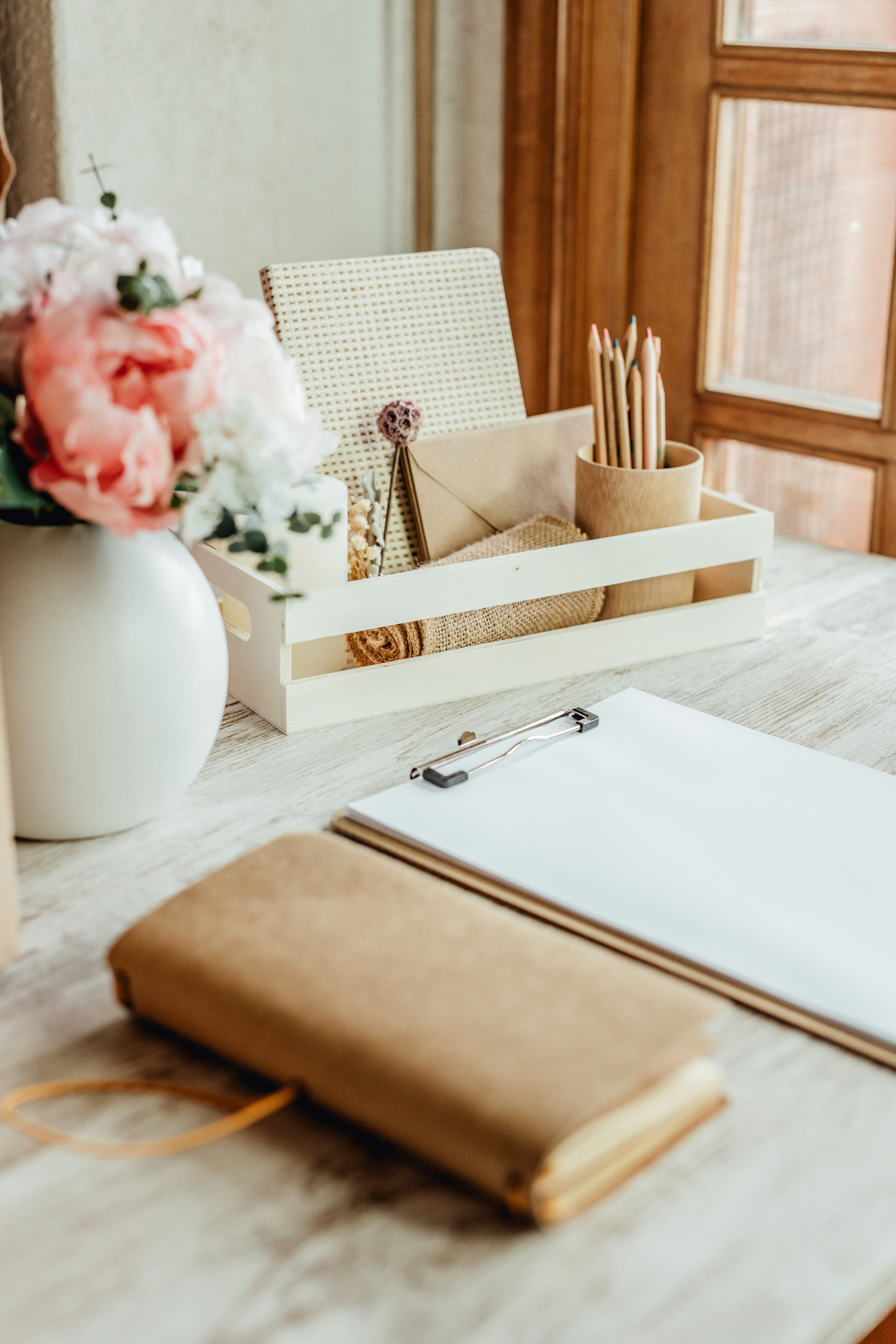 A quiet workspace with pencils, leather notebook, and pale flowers